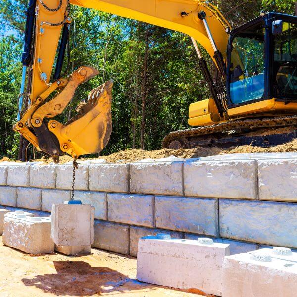 Retaining wall construction in Western Sydney with excavator lifting concrete blocks for stable wall installation by West Sydney Landscapes.